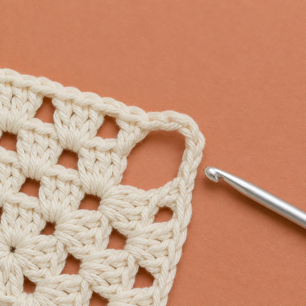 AI-assisted close-up showing a crochet hook aimed at the large open corner chain space of a granny square.